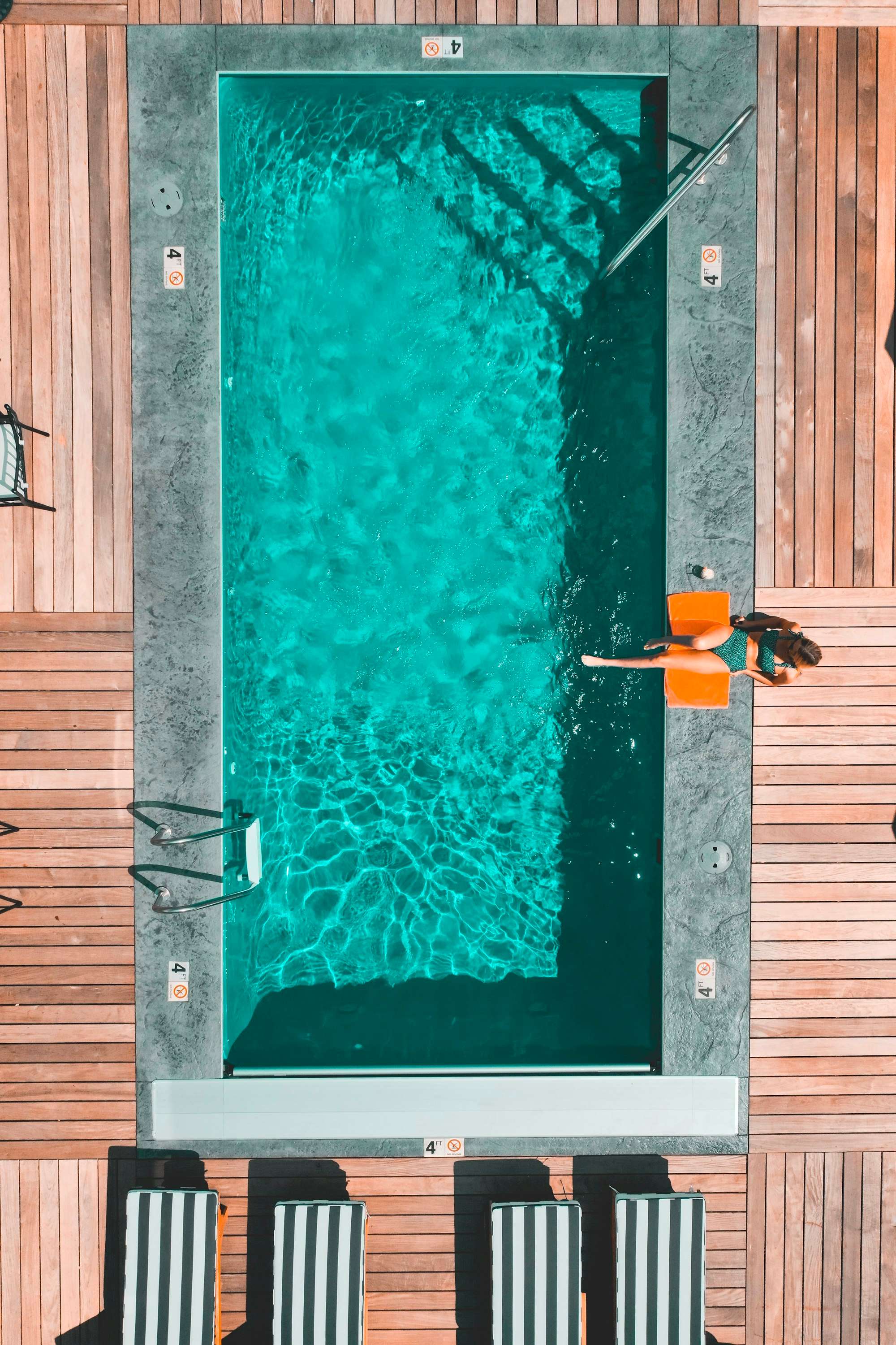 Vue aérienne d’une piscine rectangulaire turquoise entourée d’une terrasse en bois