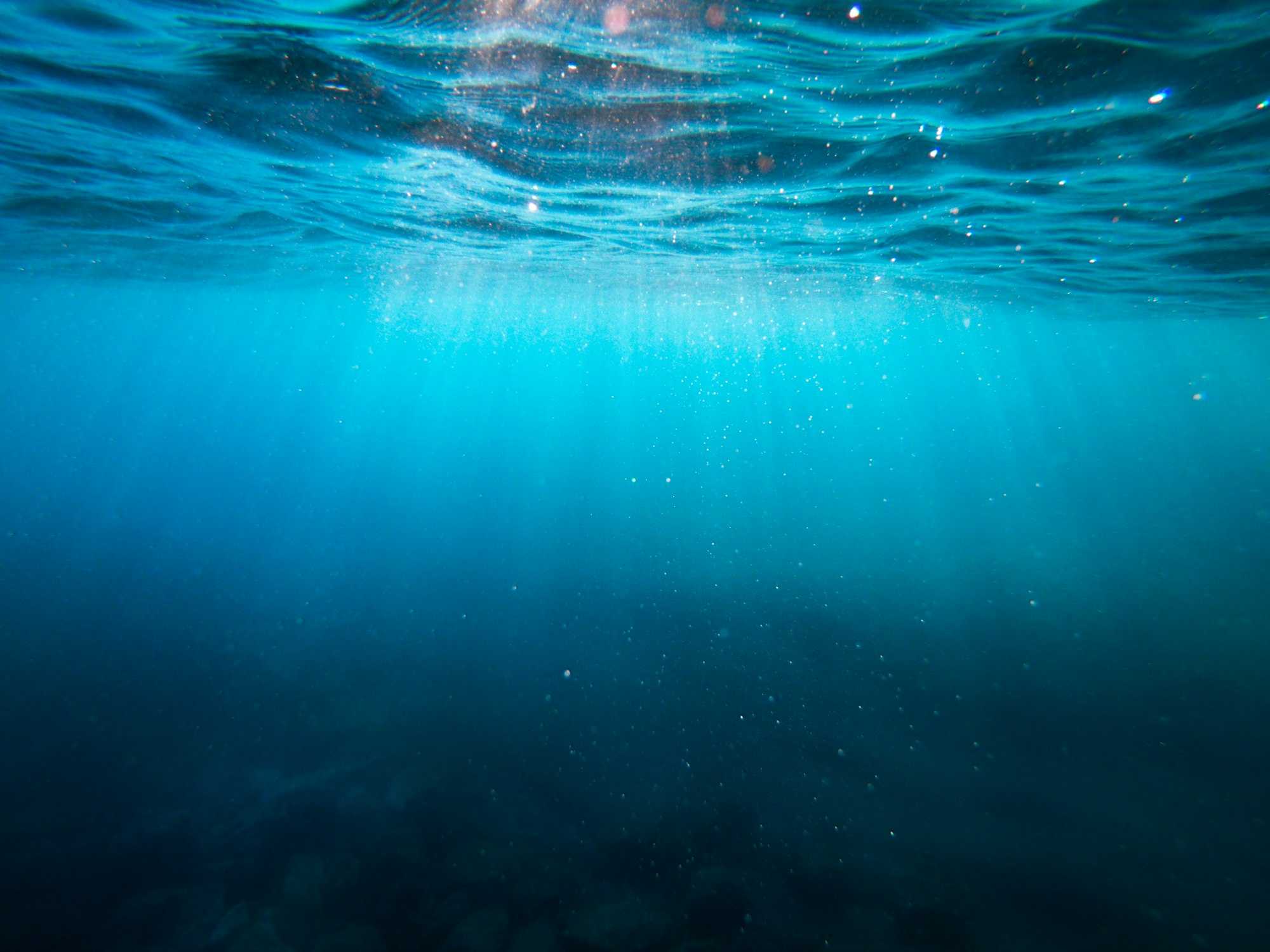 Vue sous l’eau d’une piscine, rayons de lumière traversant la surface