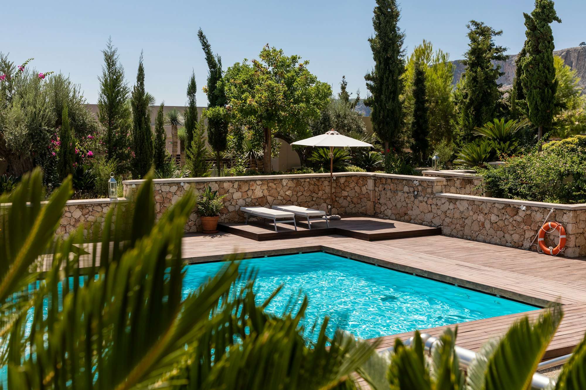 Piscine enterrée rectangulaire entourée d’un jardin méditerranéen et de cyprès